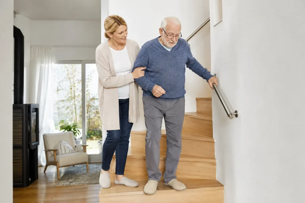 Betreuungskraft begleitet älteren Senior sicher an einer Treppe mit Handlauf im modernen Zuhause.