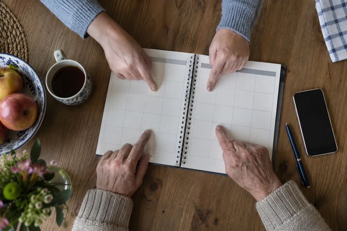 Zwei Hände tragen gemeinsam Termine in einen Kalender ein